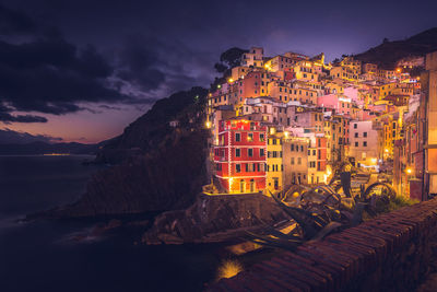 Illuminated cityscape by sea against sky at sunset