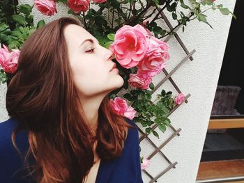 Close-up of young woman smelling pink flower against wall
