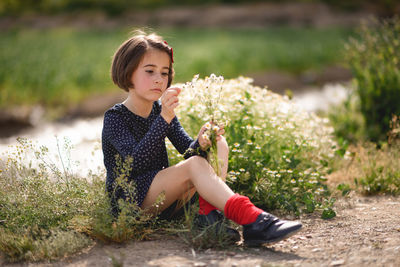 Cute girl holding flowers while sitting on field