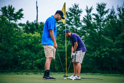 Full length of friends playing with golf course