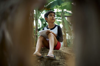 Boy writing in book while sitting outdoors