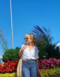 Portrait of young woman standing against blue sky