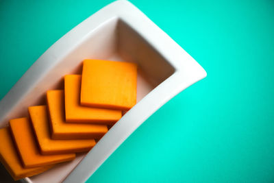 Directly above shot of cheese slices on bowl over colored background