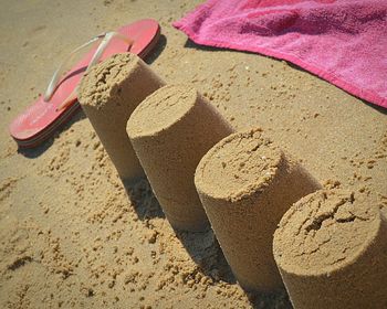 High angle view of sand castles by slipper and blanket at beach