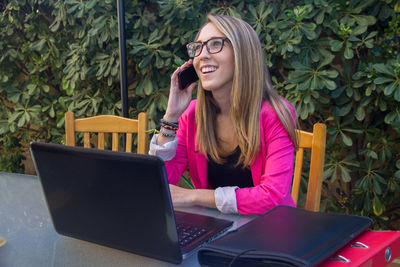 Smiling businesswoman talking on mobile phone against plants