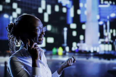 Side view of young woman looking at illuminated city at night