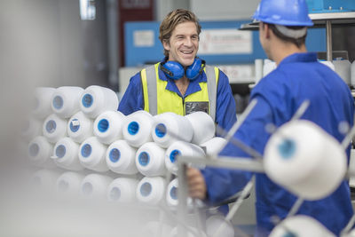 Worker wearing reflective vest smiling at colleague in factory