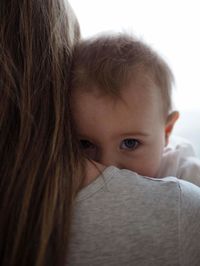 Close-up portrait of cute baby girl carried by mother at home