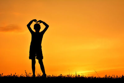 Silhouette woman standing on field against orange sky