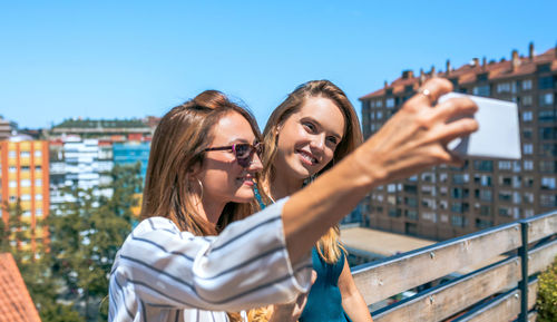 Two female friends taking a selfie in rooftop city on a summer day