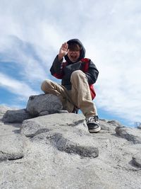 Low angle portrait of happy boy on rock against sky