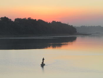 Silhouette man in lake against sky during sunset