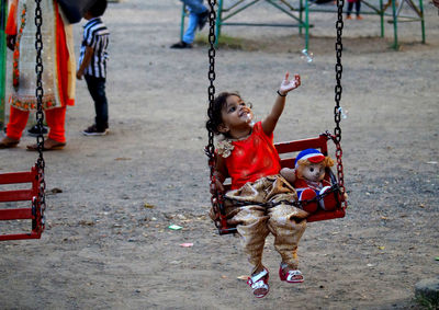 Full length of cute girl swinging at playground with bubble 