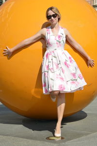 Portrait of woman leaning on large yellow ball at footpath