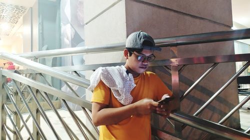 Young man using mobile phone while standing on railing