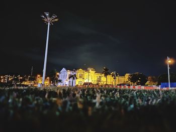 Illuminated street lights by buildings against sky at night