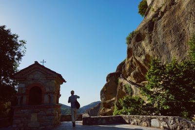 Rear view of man standing by rock against sky