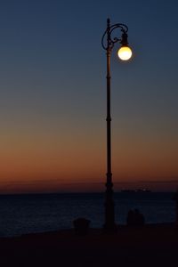 Street light by sea against sky during sunset