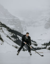 Just married groom skates with hockey stick on lake louise, alberta
