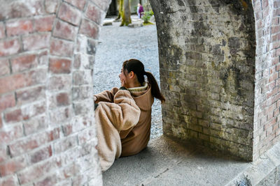 Full length of woman sitting on brick wall