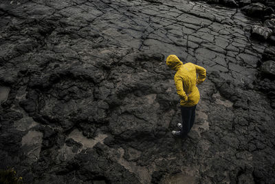 Drone shot of woman wearing raincoat while standing on rocky ground during rainy season