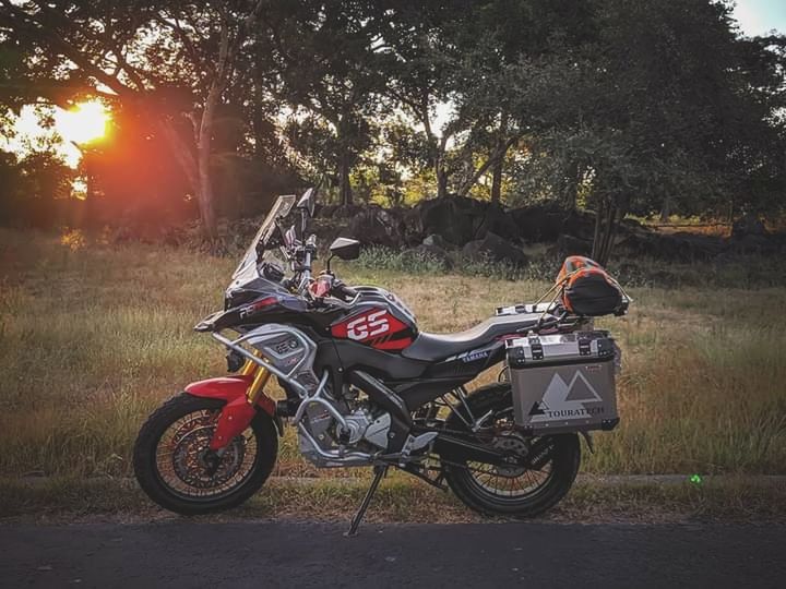 transportation, mode of transportation, tree, plant, motorcycle, nature, vehicle, land vehicle, motorcycling, helmet, sky, road, racing, sunlight, day, outdoors, sports helmet, travel, bicycle, car, sports, riding, headwear, land, leisure activity, side view, one person, full length