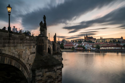 Arch bridge over river in city against sky during sunset