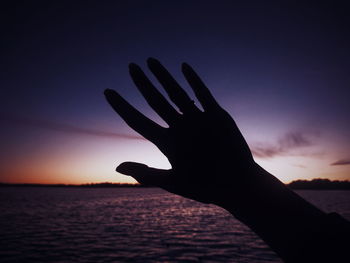 Close-up of silhouette hand against sea during sunset