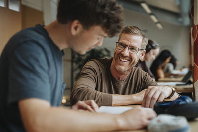 Happy professor assisting student studying in library at university