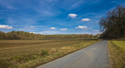 Road amidst field against blue sky