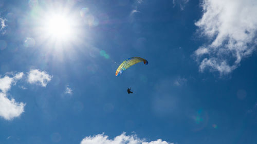 Low angle view of people paragliding against sky