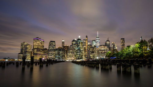 Illuminated buildings by river against sky at night