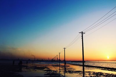 Silhouette electricity pylons on shore against clear sky during sunset