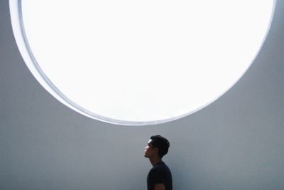 Side view of young man looking away against wall