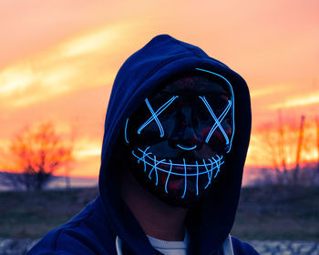 Portrait of man wearing mask against orange sky