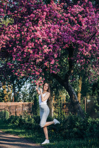 Full length of woman standing on grass by pink flower tree