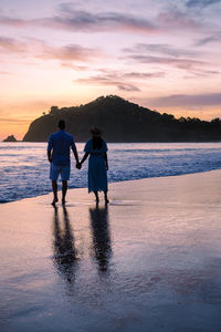 Rear view of man standing at beach against sky during sunset