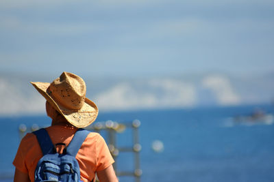 Rear view of woman wearing hat while standing against sea