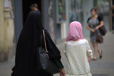 Rear view of mother and daughter in hijab standing at city street