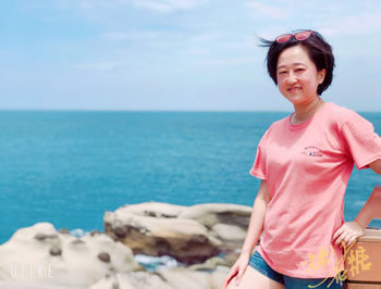 Portrait of smiling woman standing against sea against sky