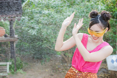 Happy young woman enjoying by sprinkler against blurred background