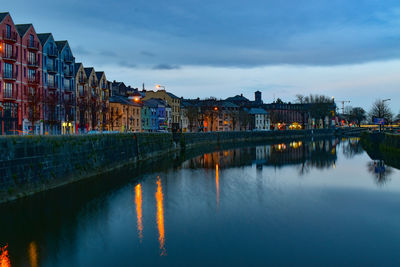 River by illuminated buildings against sky at dusk