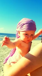 Cropped image of mother carrying baby at beach on sunny day