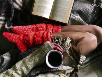 Low section of woman with coffee cup and book on bed