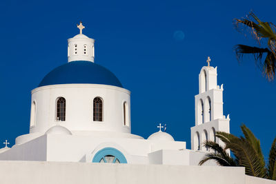 Dome and bell tower of the church of panagia platsani and the moon in oia city at santorini island