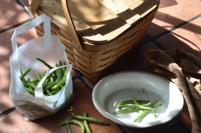 High angle view of green beans in bag by wicker basket on table