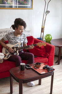 Young man playing guitar on sofa