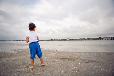 Rear boy child in blue shorts walks by the lake in summer