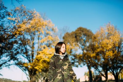 Woman in warm clothes standing against trees 