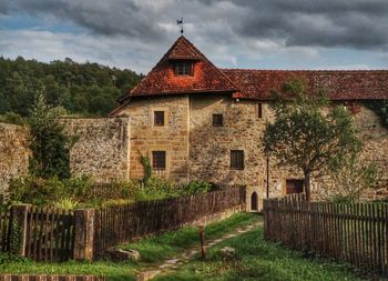 Old house on field by building against sky